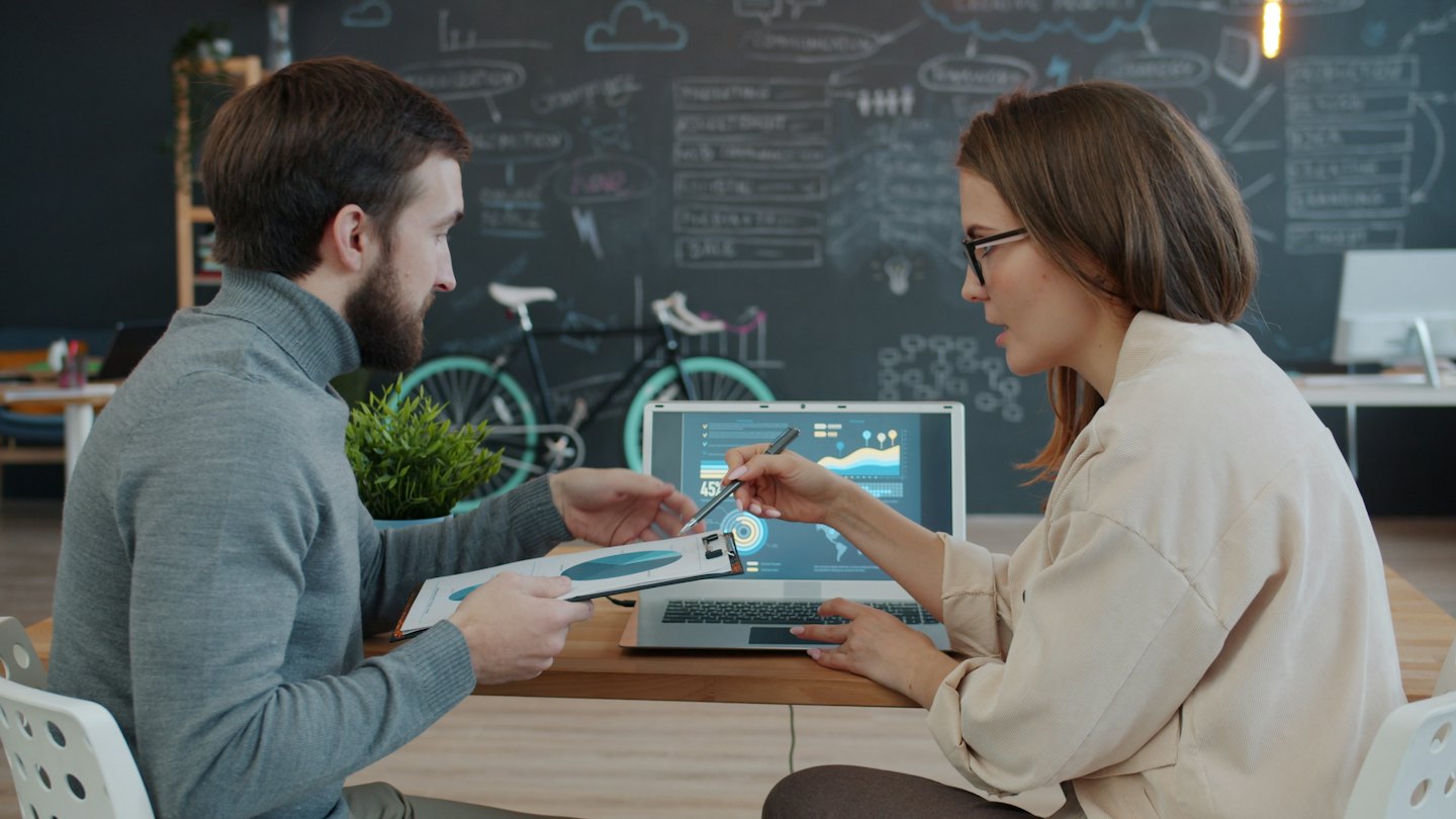 Zwei Geschäftsleute besprechen Daten auf einem Laptop und einem Dokument.